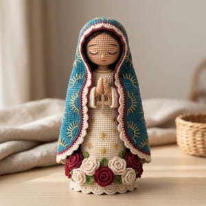 May include: A crocheted doll of the Virgin of Guadalupe featuring a cream-colored gown with gold star embroidery, a teal cloak with gold sunburst patterns, and a base adorned with red and white crocheted roses, holding a small cross pendant.