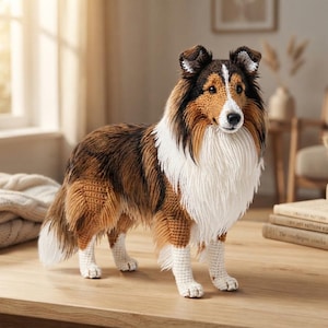 May include: A crochet figurine of a Shetland Sheepdog with a brown, black, and white coat. The dog has a white chest ruff, a white blaze on its face, and white paws. The textured yarn creates a realistic fur appearance for this standing canine.