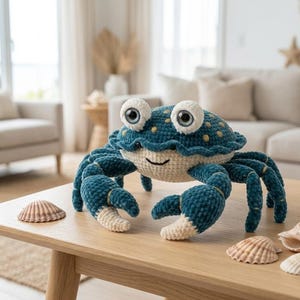 Op de afbeelding: Een gehaakt pluche krab-speeltje met een donkergroenblauw schild met lichtgele stippen, grote witte ogen met donkere pupillen en een crèmekleurige onderkant. De krab heeft twee grote scharen en meerdere poten, gemaakt van zacht, getextureerd garen.