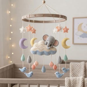 May include: A nursery mobile featuring a circular wooden frame with hanging crochet elements including a gray elephant resting on a cloud, yellow and purple crescent moons, pastel stars, blue birds, and various teardrop and diamond-shaped ornaments.