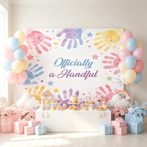 May include: A white backdrop featuring watercolor handprints in pink, purple, yellow, and blue, with the text 'Officially a Handful'. The display is framed by clusters of pastel balloons, gift boxes, and a table filled with assorted desserts.