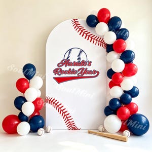 Op de afbeelding: Een witte boogvormige achtergrond met een rode honkbalstikselafbeelding en de tekst Haruto's Rookie Year. Het display is versierd met een ballonnenslinger in rood, wit en marineblauw, vergezeld door een kleine houten honkbalknuppel en ballen.