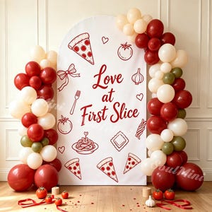 May include: A white arched backdrop featuring the red text Love at First Slice and illustrations of pizza, pasta, and garlic. The display is framed by clusters of red, cream, and olive green balloons, with fresh tomatoes and garlic on the floor.
