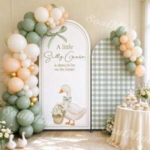 Peut inclure: Un panneau arqué blanc avec un nœud vert, une illustration d'oie et le texte A little Silly Goose is about to be on the loose, accompagné d'un panneau à carreaux verts et de guirlandes de ballons vert sauge, crème et pêche.