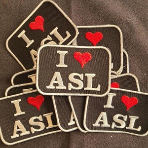 May include: A collection of rectangular embroidered patches featuring a black background with a white border. Each patch displays the text I, a red heart symbol, and the letters ASL in white, capitalized, serif font, arranged in a stacked layout.