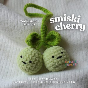 Pode incluir: Um ornamento de cereja em crochê feito de fio de chenille verde claro com duas formas de fruta redondas, cada uma com olhos pretos bordados e uma boca pequena. Inclui um caule verde com folhas e cordões ajustáveis. O texto diz smiski cherry.