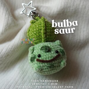 Peut inclure: Un porte-clés en crochet vert représentant une créature avec une structure végétale sur le dos, des yeux en perles noires et une bouche cousue marron. Il possède un fermoir étoile argenté. Texte : bulba saur, 100% HANDMADE, LENGTH: +-8 CM, MATERIAL: PREMIUM VELVET YARN.