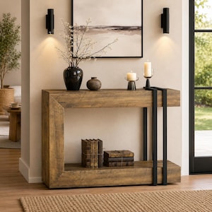 May include: A rectangular console table with a wood grain finish and a black metal frame. The table features a lower shelf holding two stacks of books. On the top surface are a black vase with white branches, a small brown vase, and two candles.