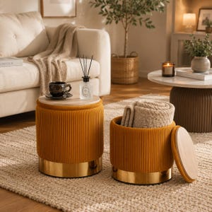 May include: Two round mustard yellow velvet ottomans with vertical channel tufting and gold metal bases. One ottoman features a light wood lid top, while the other has its lid removed to reveal a beige textured throw blanket stored inside.