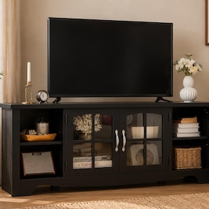 May include: A black rectangular media console featuring two central glass-paneled doors with silver handles, flanked by open shelving on both sides. The unit supports a large flat-screen television and provides storage for books, decor, and baskets.