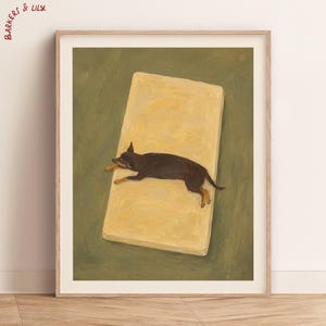 May include: A framed art print titled BARKERS & LILY featuring a painting of a small black and tan dog lying flat on a rectangular yellow mat against a solid olive green background. The dog is positioned centrally on the mat.