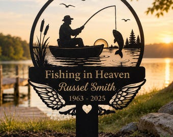 May include: A black metal garden stake featuring a circular silhouette of a person fishing from a boat. The text reads Fishing in Heaven, Russel Smith, and 1963-2025. The design includes cattails, birds, a sun, and decorative angel wings.