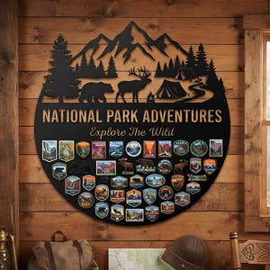 May include: A circular black metal wall sign featuring a mountain, forest, bear, elk, and tent silhouette. The text reads "NATIONAL PARK ADVENTURES" and "Explore The Wild". The lower section displays numerous colorful national park patches.
