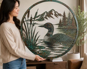 Puede incluir: Una pieza de arte mural circular de metal que presenta una escena recortada detallada de un colimbo nadando en un lago. El diseño incluye espadañas en primer plano, una cordillera al fondo y un bosque de pinos, todo con un acabado de pátina de cobre y verde azulado.