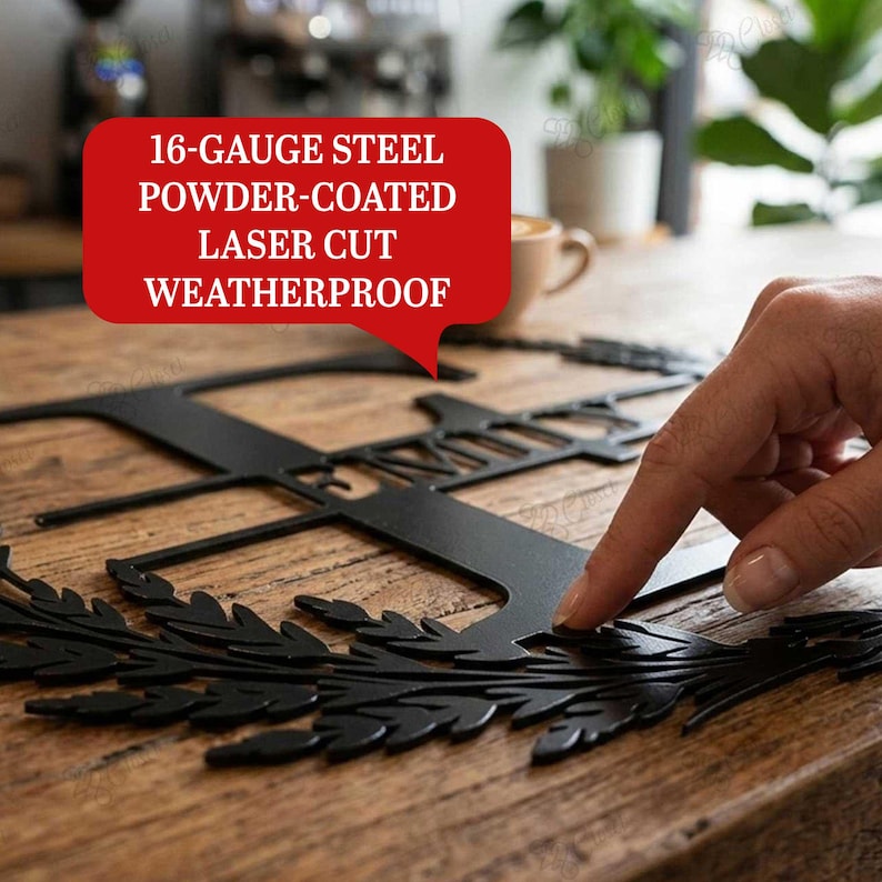 May include: A black metal monogram sign featuring a laser-cut letter and decorative leaf accents. The sign is made of 16-gauge steel, powder-coated, and weatherproof. The design includes a large letter with intricate foliage details.