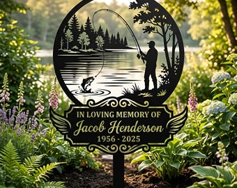 May include: A black metal garden stake featuring a circular cutout of a person fishing by a lake with trees. Below the circle is a decorative plaque with wings that reads IN LOVING MEMORY OF Jacob Henderson 1956 - 2025 in gold lettering.