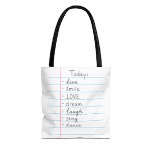 Op de afbeelding: Een witte tote bag met zwarte hengsels voorzien van een gelinieerd papierontwerp. De tekst luidt: Today: - live - smile - LOVE - dream - laugh - sing - dance. De print bootst een notitieboekpagina na met blauwe lijnen en een rode kantlijn.