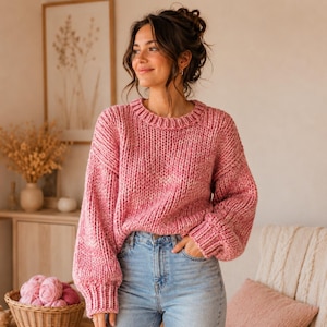 May include: A chunky knit sweater in a variegated pink and white yarn featuring a crew neckline, dropped shoulders, and long sleeves with ribbed cuffs. The sweater is paired with light blue denim jeans with a visible metal button and zipper.