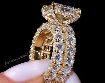May include: A gold ring featuring a large rectangular radiant-cut center stone set in a basket with small pavé diamonds. The band consists of two rows of round brilliant-cut stones set in gold. The text Aexora Jewells is visible on the side.
