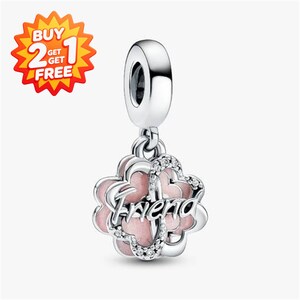 May include: A silver charm pendant featuring a flower shape with light pink enamel petals and a central silver script word that reads "friend". The charm is accented with small clear stones along the edges and includes a silver bail at the top.