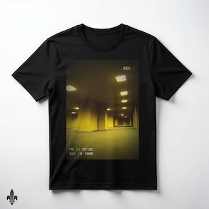 May include: A black t-shirt featuring a rectangular graphic print of a dimly lit, yellow-toned indoor space with square ceiling lights. The graphic includes a red recording dot, the text REC, and a timestamp reading PM 11:37:21 MAY 19 1996.