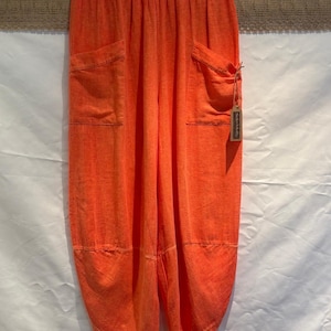 May include: Bright orange trousers featuring an elasticated waistband, two large front patch pockets, and a relaxed, tapered leg silhouette. A small rectangular tag with the text Solo-Molly is attached to the right pocket with a thin string.