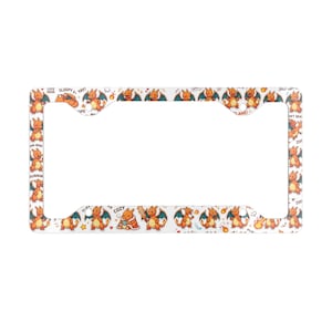 May include: A white rectangular license plate frame featuring a repeating pattern of orange dragon-like creatures in various poses. The design includes small text elements like "SLEEPY", "YAY", "NOM", "RUNNING", "COZY", and "FLAME" scattered among the characters.