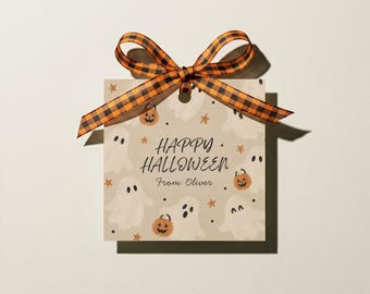 May include: A square gift tag featuring a beige background with a pattern of white ghosts, orange jack-o'-lanterns, and small stars. The text reads "HAPPY HALLOWEEN" and "From: Oliver". An orange and black buffalo plaid ribbon is tied at the top.