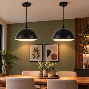 May include: Two matte black dome-shaped pendant lights with thin black cords and circular ceiling mounts. The fixtures feature a smooth, rounded exterior finish and a wide opening at the bottom, casting a warm, downward-facing light.