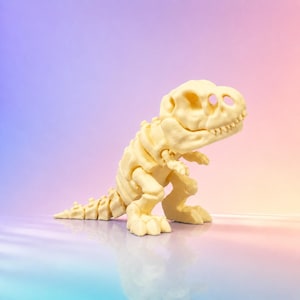 Puede incluir: Una figura de esqueleto de Tyrannosaurus rex articulada de color crema. El modelo de dinosaurio presenta un cráneo grande con dientes visibles, una columna vertebral segmentada, una cola larga y dos extremidades delanteras pequeñas.