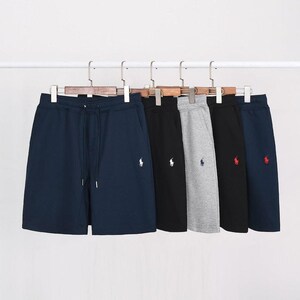 Può includere: Una collezione di cinque pantaloncini in cotone appesi a grucce di legno. I pantaloncini sono disponibili in blu navy, nero, grigio chiaro e blu scuro, ognuno con un logo ricamato di un giocatore di polo sulla gamba sinistra e coulisse in vita.
