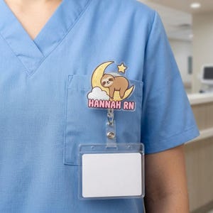Könnte beinhalten: Ein Ausweishalter mit einem Faultier-Cartoon, das auf einem gelben Halbmond mit einem kleinen Stern und einer weißen Wolke ruht. Unter dem Mond ist der Text HANNAH RN in rosa Buchstaben gedruckt. Ein horizontaler Ausweishalter ist befestigt.