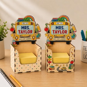 Könnte beinhalten: Zwei Schreibtisch-Organizer aus Holz in Form von gelben Schulbussen mit der Aufschrift "MRS. TAYLOR" und "NEXT STOP: LEARNING". Sie haben eine helle Holzoberfläche mit bunten schulbezogenen Grafiken und enthalten gelbe Haftnotizen.