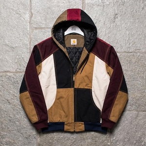Puede incluir: Una chaqueta con capucha de bloques de color con un diseño de patchwork en tonos tostado, negro, burdeos y crema. La chaqueta tiene cierre de cremallera frontal, forro interior negro acolchado, puños acanalados y una etiqueta de Carhartt.