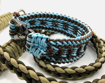 May include: A pet collar and leash set crafted from woven paracord. The collar features a light blue and dark brown braided pattern with a black metal buckle. The leash is constructed with a braided design in olive green and tan cord.