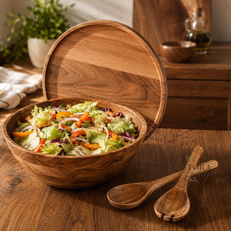 Puede incluir: Un cuenco de madera redondo lleno de una mezcla fresca de lechuga verde, cebolla roja en rodajas y tiras de pimiento naranja. Una tapa circular de madera a juego se apoya verticalmente detr&aacute;s del cuenco, junto a dos cubiertos de madera.