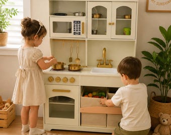 Puede incluir: Una cocina de juguete de madera color crema que incluye un microondas con pantalla digital que muestra 08:35, un fregadero con grifo dorado, una estufa de dos quemadores, un horno y dos cajones de almacenamiento inferiores con frutas y verduras de juguete.