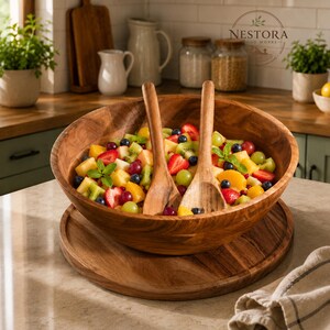 Puede incluir: Un cuenco de madera grande y redondo para ensalada con una bandeja de madera a juego debajo y dos cubiertos de madera para servir. El cuenco est&aacute; lleno de una colorida ensalada de frutas con fresas, ar&aacute;ndanos, kiwi y mango.