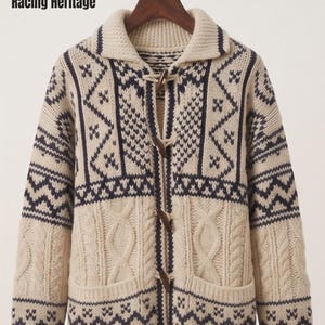 May include: A cream-colored knit cardigan featuring dark navy blue geometric patterns, a wide collar, and four wooden toggle closures. The front displays vertical cable knit panels and two patch pockets, with the text Racing Heritage printed in black.