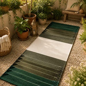 May include: A rectangular runner rug featuring a color-blocked design with a wide central cream-colored stripe flanked by sections of dark forest green and olive green. The rug is finished with decorative tassels along the short edges.