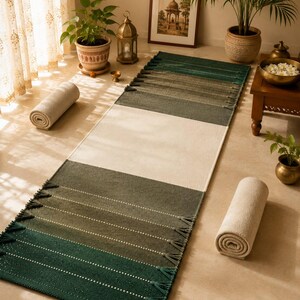 May include: A rectangular runner rug featuring a color-blocked design with a large central cream section flanked by gradient panels in shades of olive and forest green. The rug is finished with decorative tassels along the short edges.