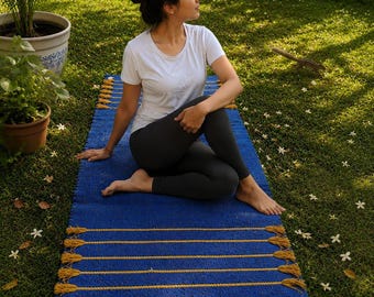 May include: A rectangular blue yoga mat featuring horizontal yellow braided rope accents with tassels at each end. The mat has a textured surface and is designed for exercise, providing a stable base for various physical activities and movements.