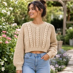Può includere: Un maglione corto color beige a maniche lunghe con un motivo a maglia testurizzato, colonne verticali a trecce sul davanti, scollo rotondo a coste e polsini a coste, abbinato a jeans in denim azzurro con chiusura a bottone.