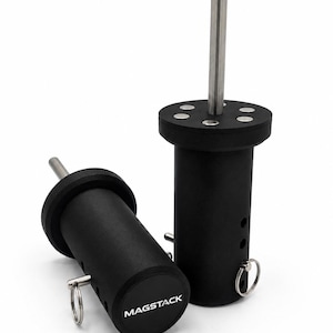 May include: Two black cylindrical Magstack tools with a matte finish. Each tool features a central vertical silver metal rod, a flat top with embedded silver circular accents, and a side-mounted silver ring pin. The base is labelled Magstack.