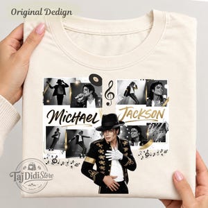 May include: A cream-coloured t-shirt featuring a collage of black and white photographs of Michael Jackson. The design includes the text "Michael Jackson" in gold script, musical notes, a vinyl record, and a central image of the artist in a black fedora.
