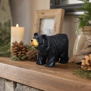 Könnte beinhalten: Eine schwarze Bärenfigur mit geschnitzter, facettierter Textur und einer glatten, hellen Schnauze. Der Bär steht in einer vierbeinigen Position und zeichnet sich durch dunkle Augen und ein markantes, kantiges Design aus, das die Holzoptik betont.