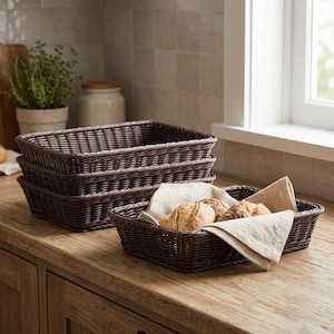 May include: A set of rectangular dark brown woven baskets with a stack of three empty baskets and one basket in the foreground containing a light beige linen cloth and several small, round, golden-brown baked bread rolls.