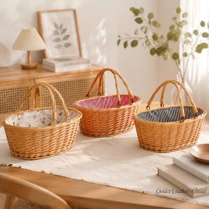 May include: Three oval-shaped woven wicker baskets with arched handles. The left basket features a white fabric liner with a floral pattern, the center basket has a red and white striped liner, and the right basket has a blue and white striped liner.
