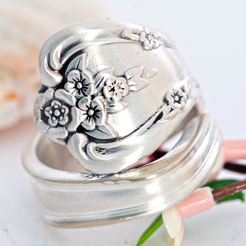 May include: A silver spoon ring with a floral design. The ring is made from a vintage spoon and features a cluster of flowers with intricate details.