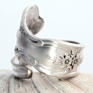 May include: A silver spoon ring with a floral design. The ring is made from a bent spoon and has a unique, handmade look.